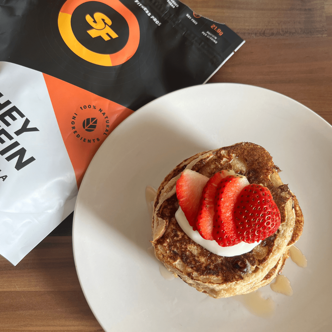 Stack of protein pancakes on a white plate, topped with strawberries